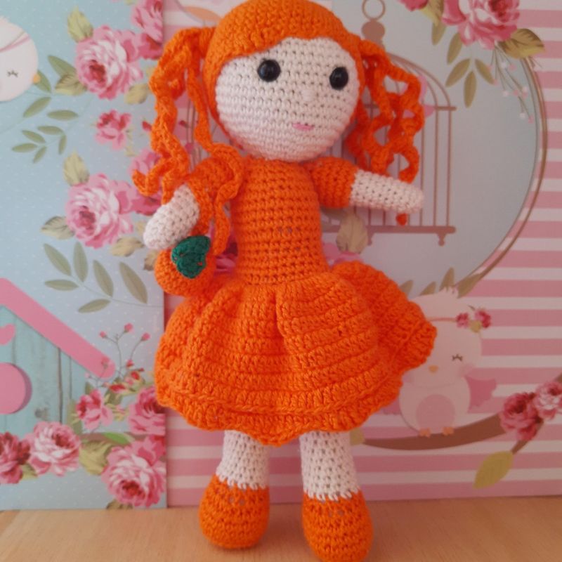Uma boneca de crochê com uma roupa laranja nas folhas